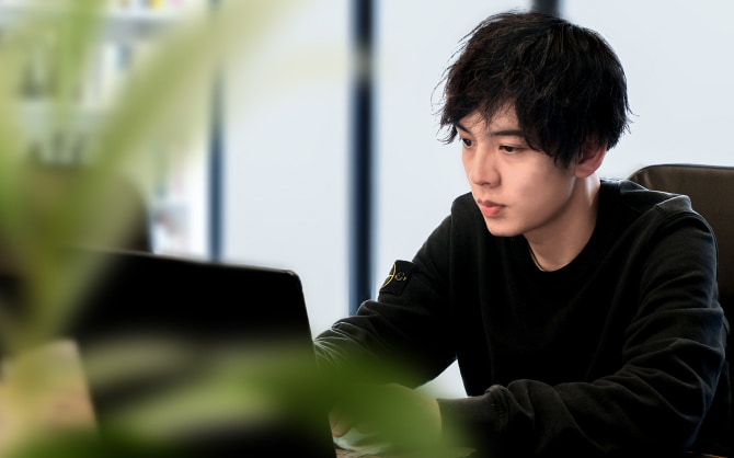 ノートパソコンで作業する男性社員。オフィスのデスクに座り、真剣な表情で画面を見つめている